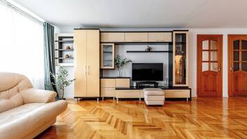 A modern living room with a sofa, TV, wooden herringbone floor, and built-in shelving.