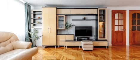 A modern living room with a sofa, TV, wooden herringbone floor, and built-in shelving.