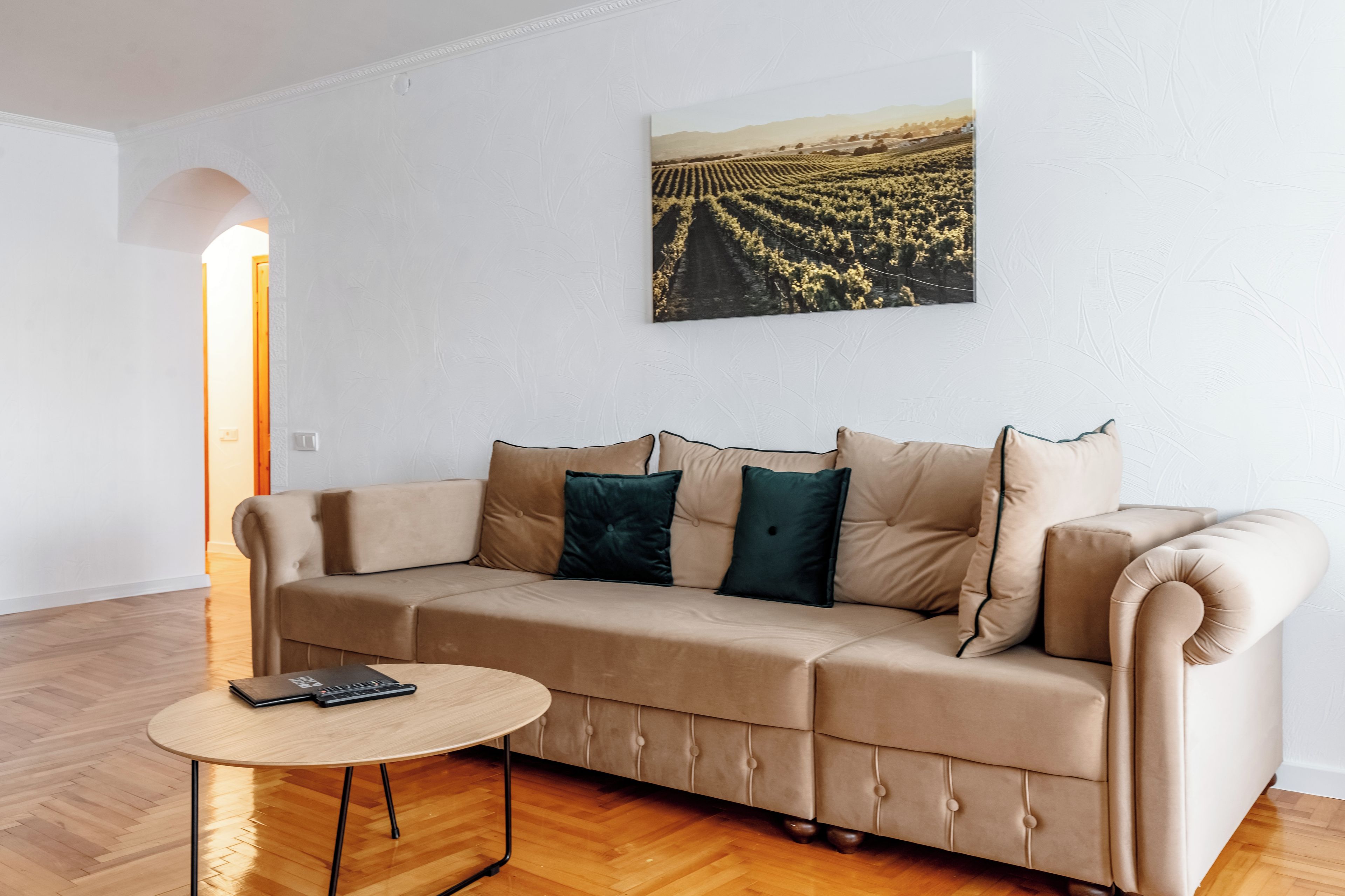 A living room with a beige sofa, a round wooden table, and a landscape painting on the wall.