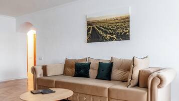 A living room with a beige sofa, a round wooden table, and a landscape painting on the wall.