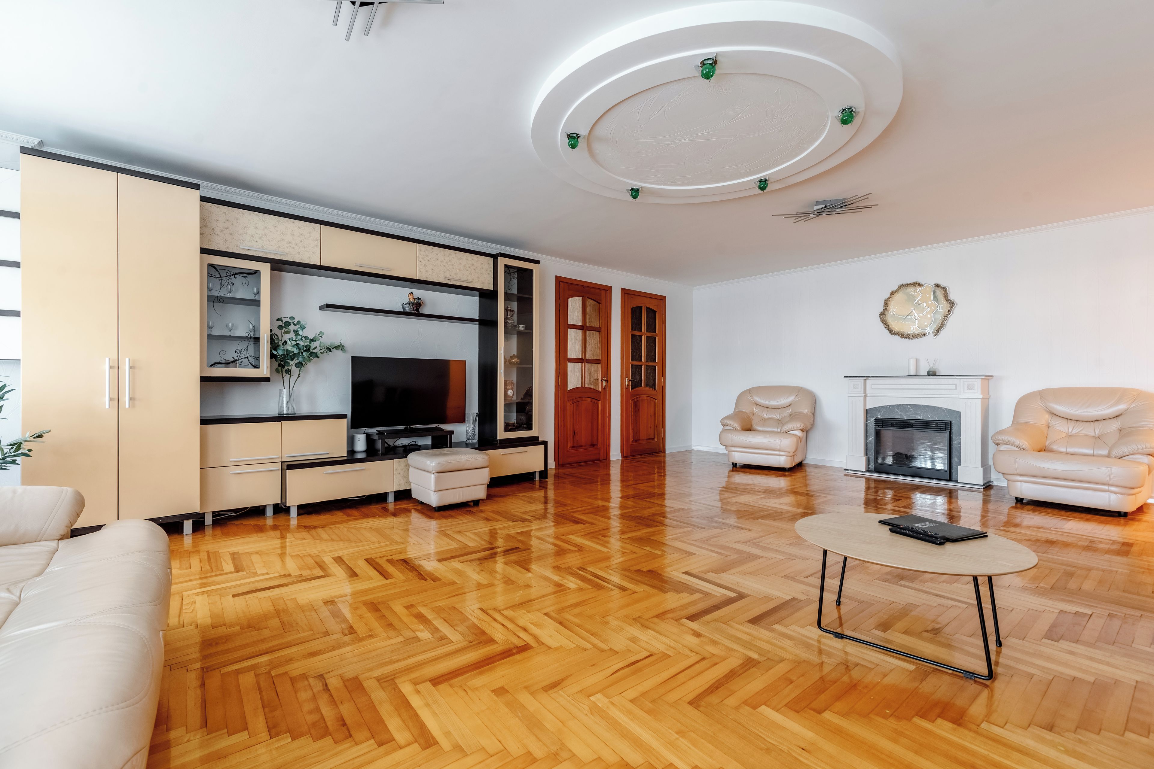 A modern living room with a herringbone wood floor, a flat-screen TV, a fireplace, and two leather armchairs.
