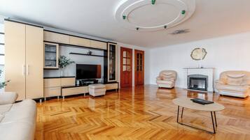 Uma sala de estar moderna com piso de madeira em padrão herringbone, uma TV de tela plana, uma lareira e duas poltronas de couro.