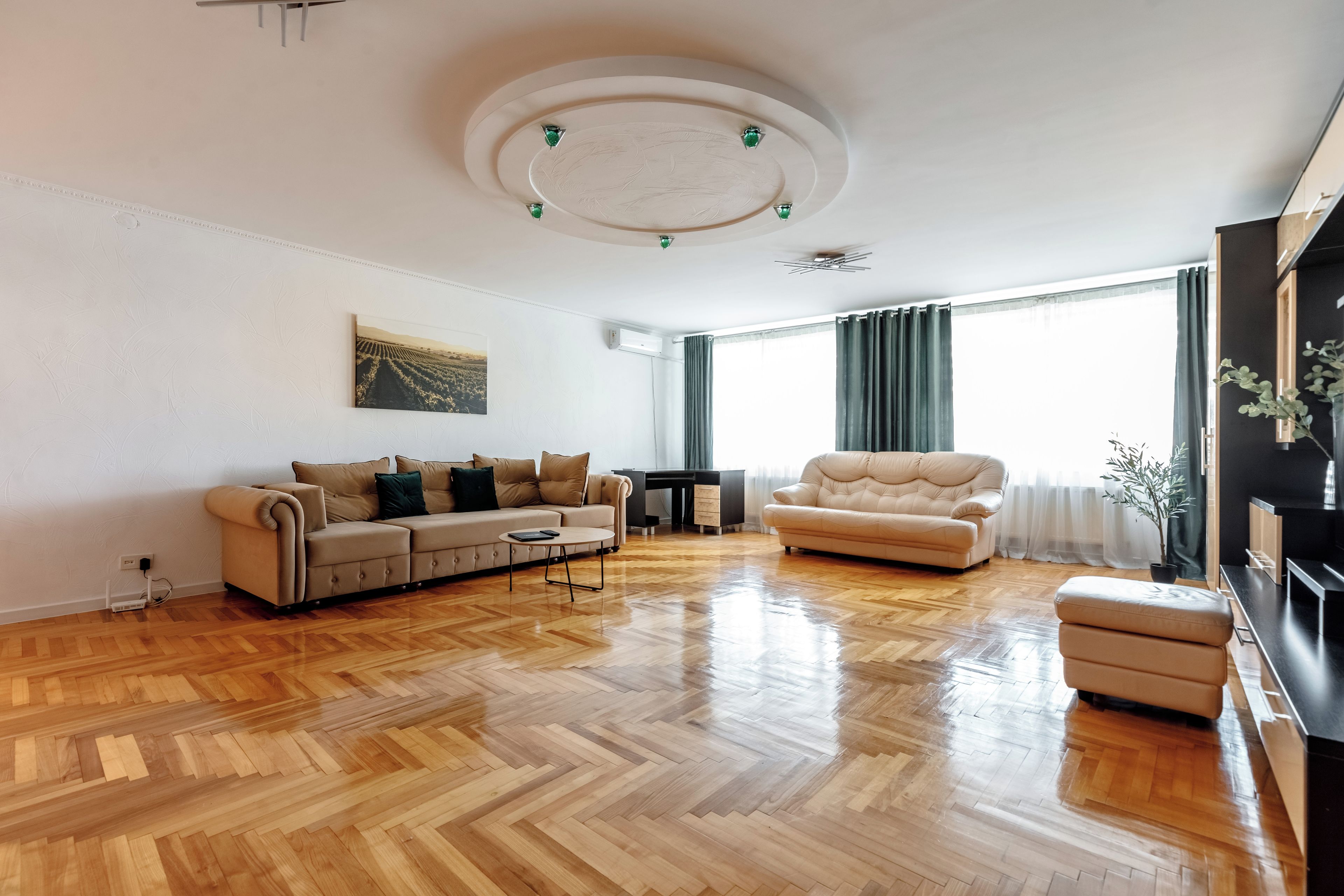 A spacious living room with a herringbone wooden floor, a beige sofa, a leather armchair, and a coffee table.