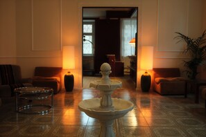 A lobby with a central fountain, seating areas, and lamps. - Hotel DEDE (Augsburg)