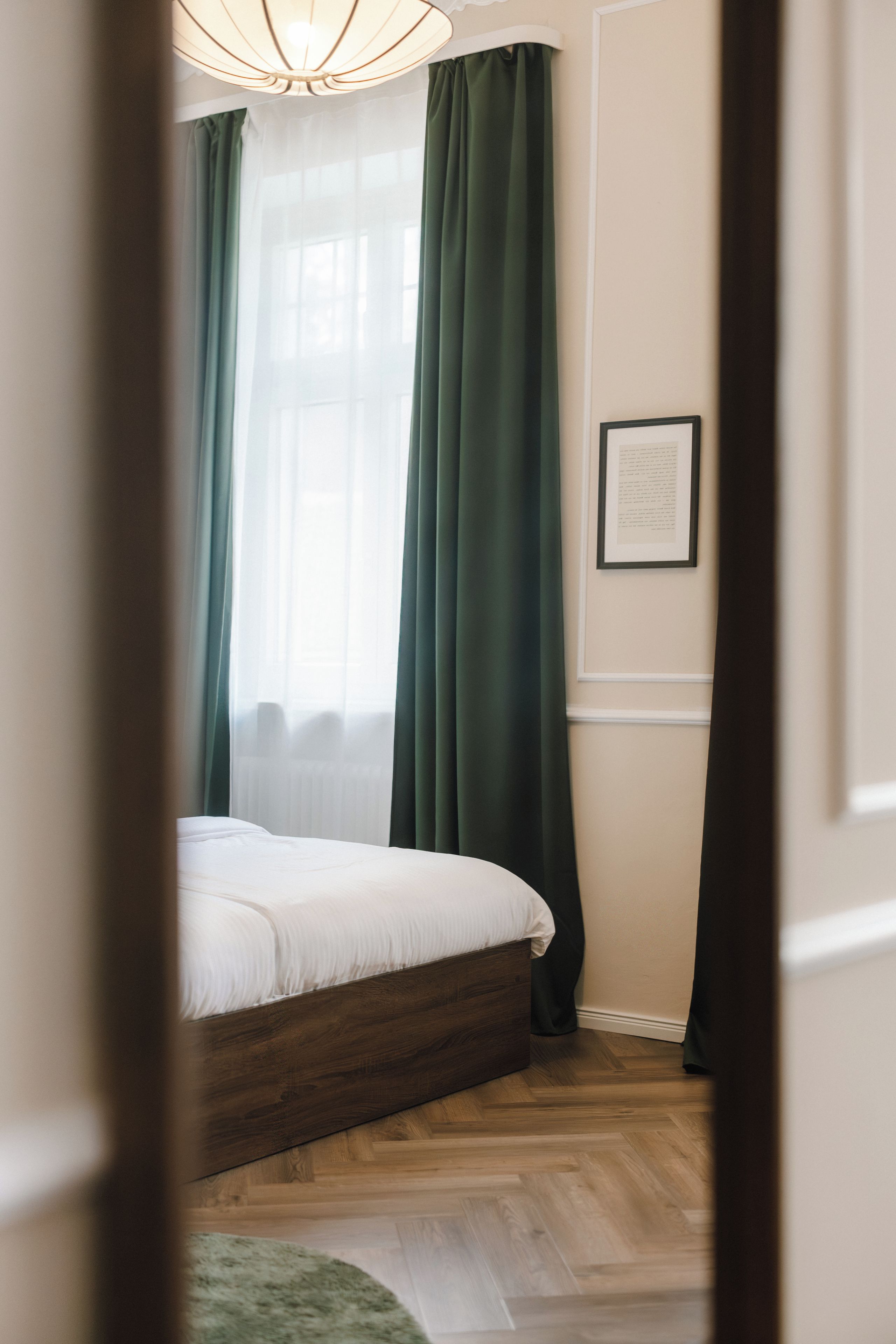 Un dormitorio con una cama, cortinas, un cuadro en la pared y suelo de madera.