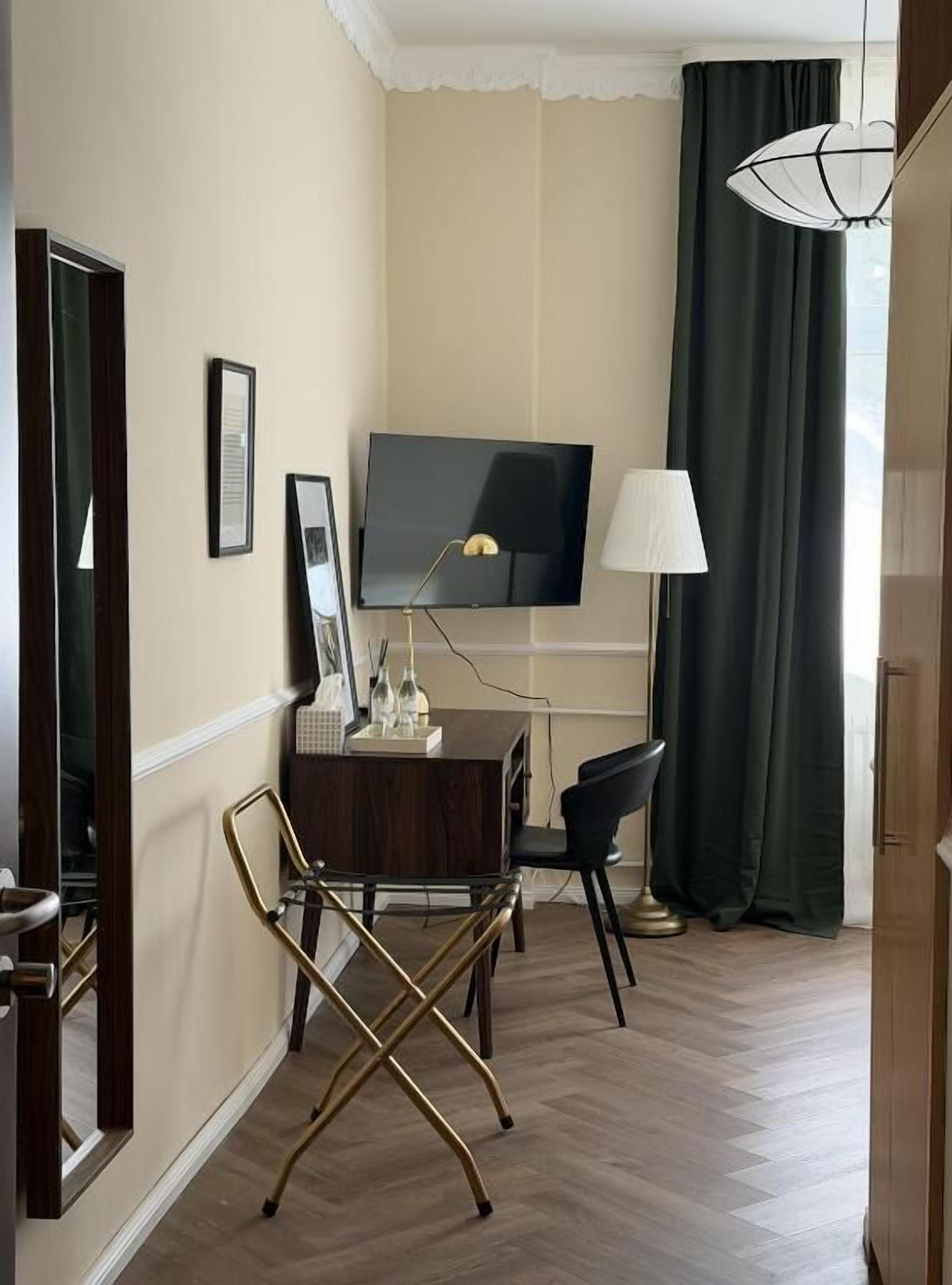 Habitación de hotel con televisión de pantalla plana, escritorio con lámpara, una silla y una butaca de respaldo cruzado.