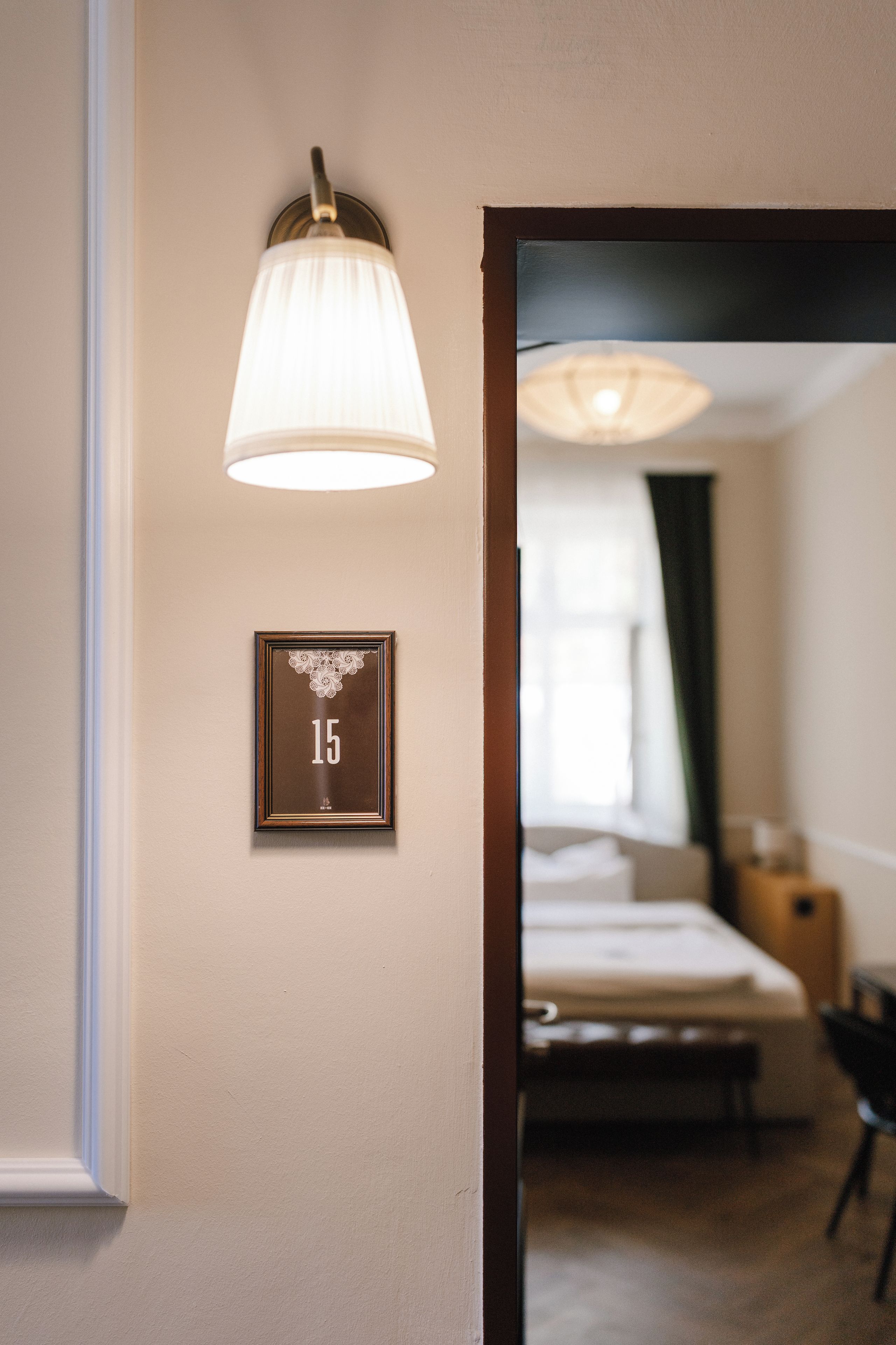 A hotel room with a bed, a bedside table, and a wall-mounted light fixture.