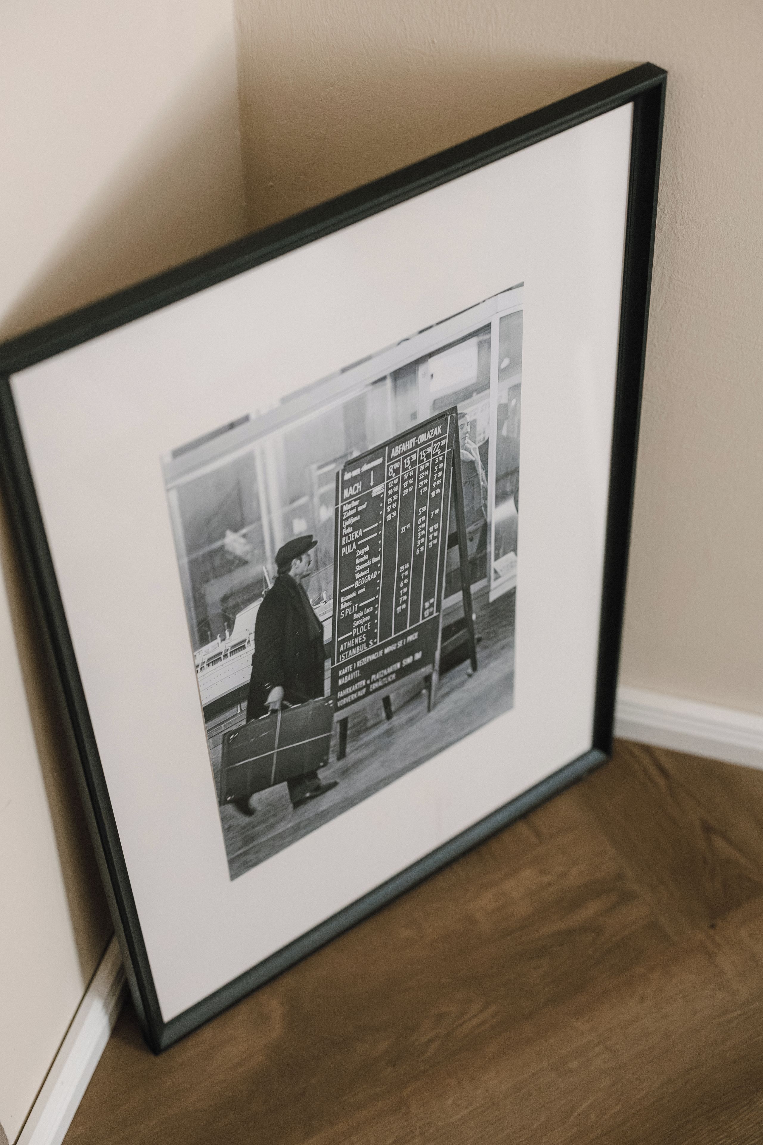 A framed photograph of a vintage bus timetable with a man standing beside it.