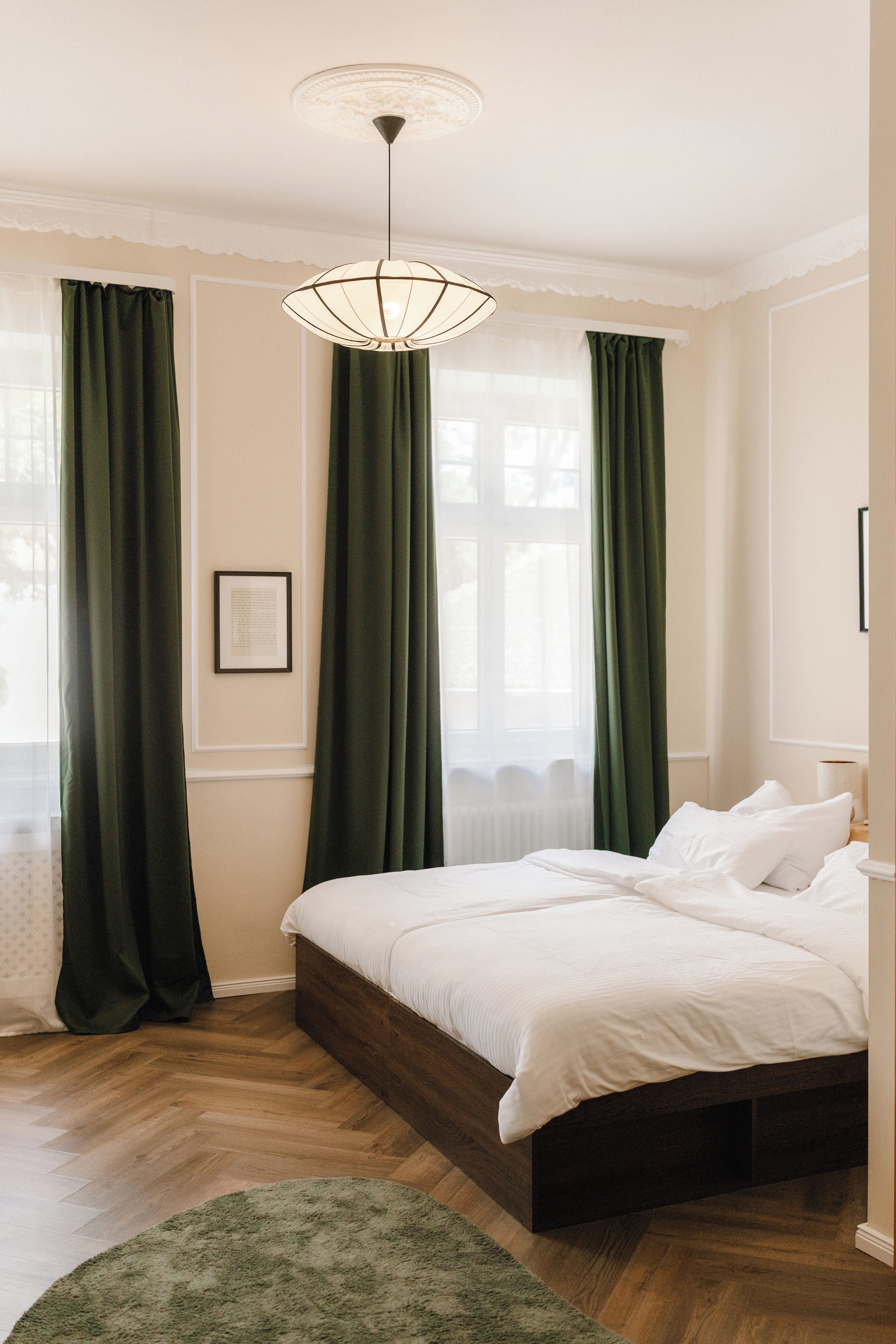 Ein Schlafzimmer mit einem großen Bett, einer hängenden Lampenleuchte und grünen Vorhängen.