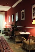 Una habitación con pared roja, una mesa redonda, sillas de mimbre, una planta en maceta y una alfombra estampada.