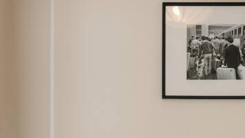 Una cama bien hecha con sábanas y almohadas blancas, una lámpara de noche y una fotografía blanco y negro en la pared.