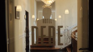 Entrada de un hotel con un candelabro, una escalera y un cartel que dice 'HOTEL DERE'.