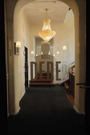 A hotel entrance with a chandelier, a staircase, and a sign reading 'HOTEL DERE'.