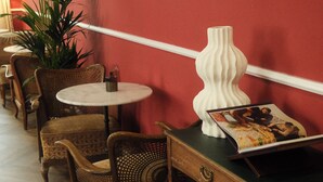 A hotel lobby with red walls, framed pictures, a white vase, and wicker chairs. - Hotel DEDE (Augsburg)