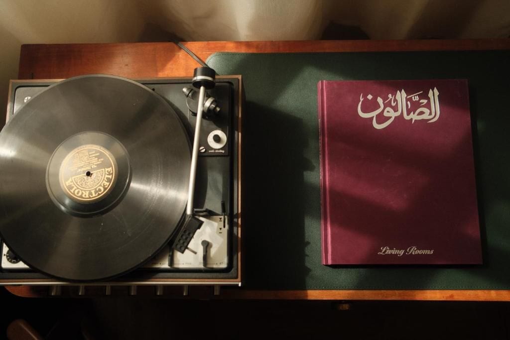 Tocadiscos con un disco de vinilo y un libro titulado 'Living Rooms' sobre una superficie de madera.