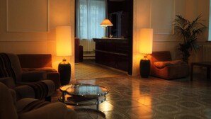 Vestíbulo de hotel con piano, dos lámparas, una mesa de centro de cristal y una planta.