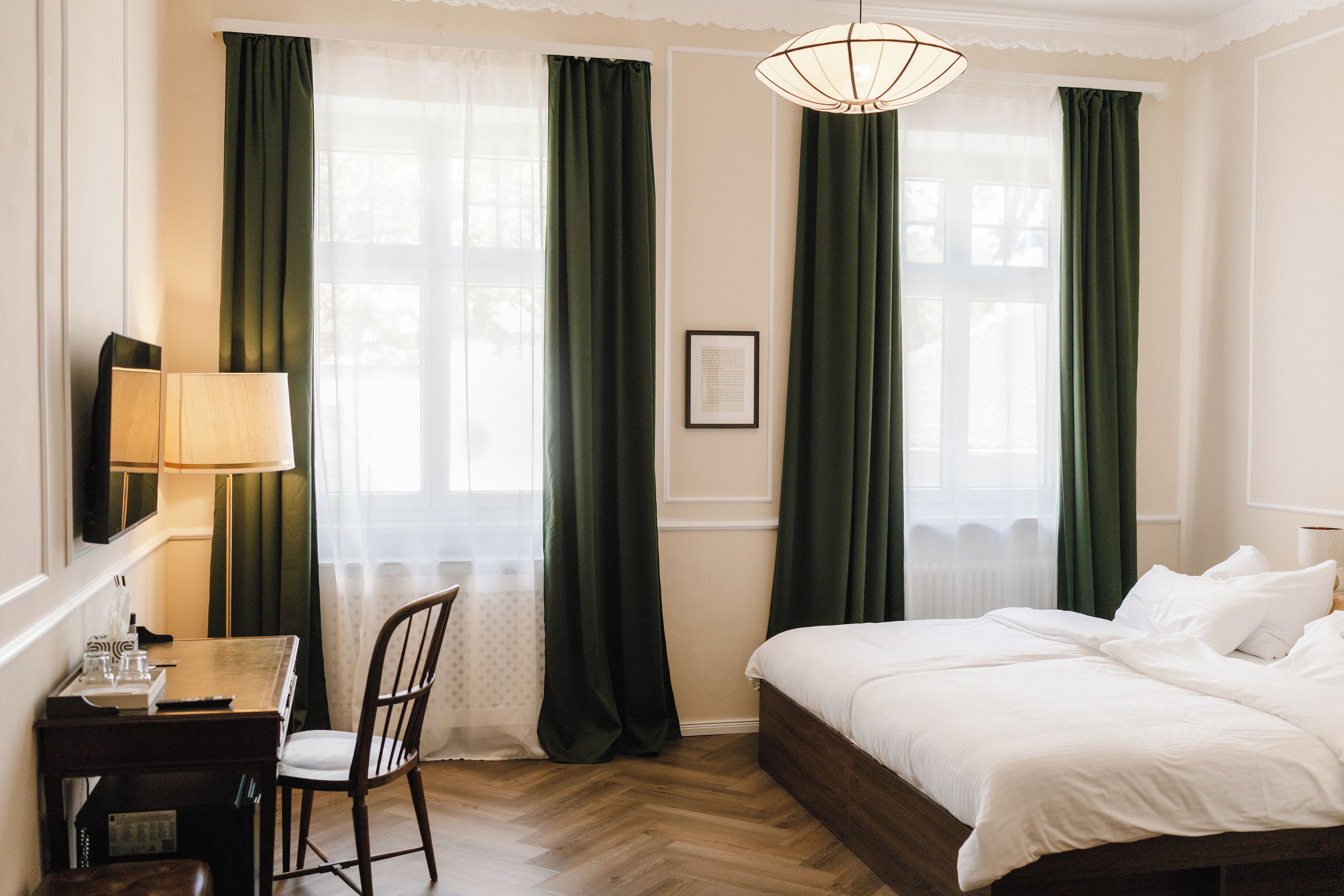 A hotel room with a bed, a desk, a chair, and a lamp.