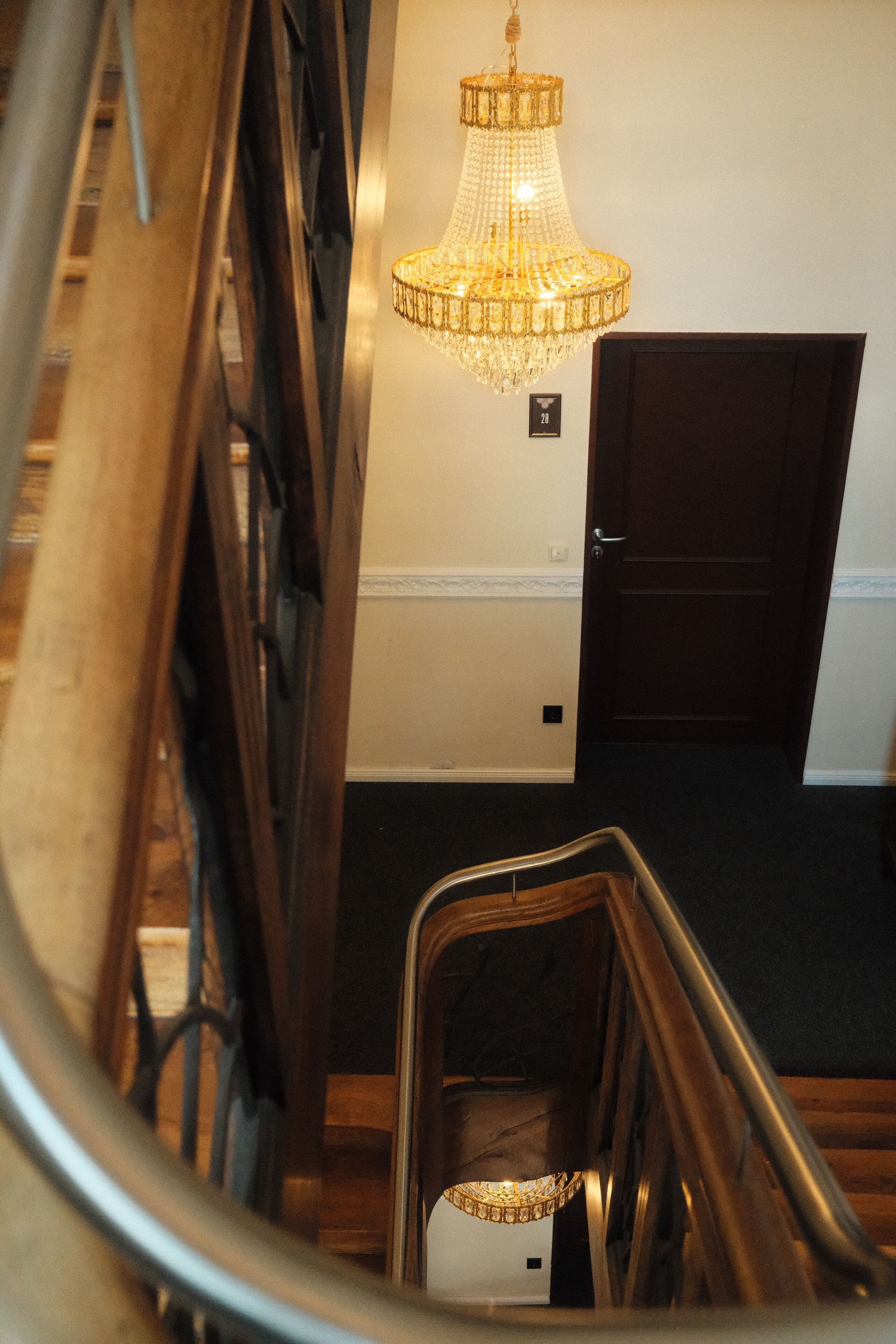 A staircase with a handrail, a chandelier, and a door with a number sign above it.
