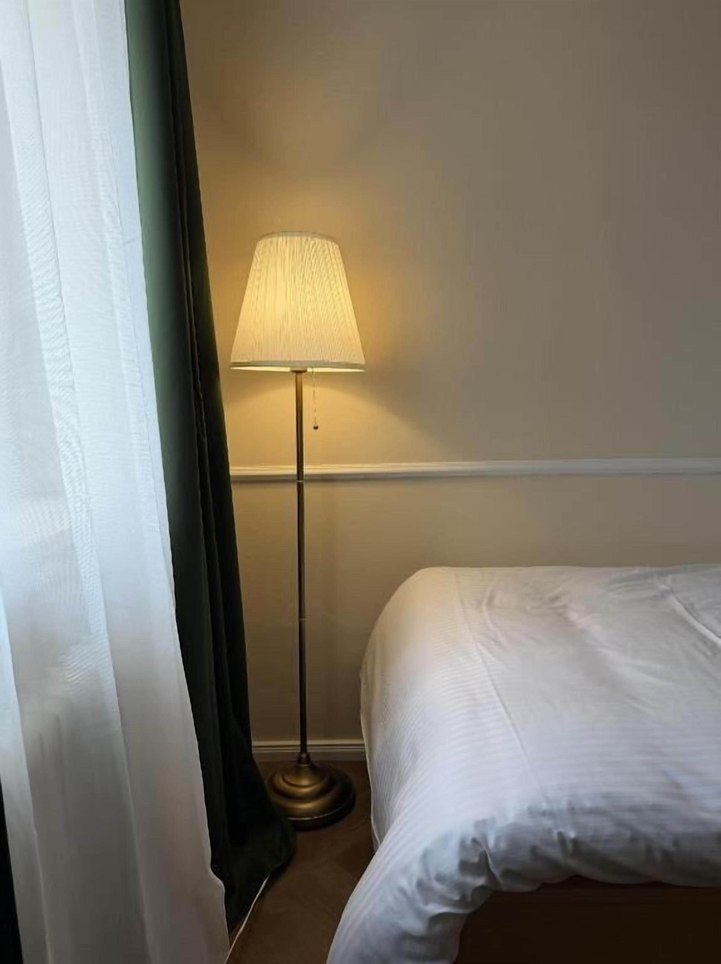 Ein Hotelzimmer mit Bett, Stehlampe und Vorhang.