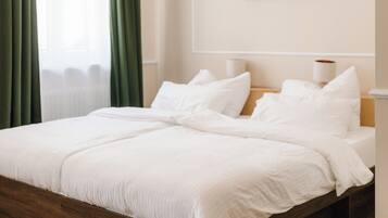 Una cama bien hecha con sábanas blancas en una habitación con piso de madera, una cortina verde y un cuadro enmarcado en la pared.