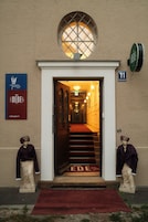 Entrada de un hotel con alfombra roja, una escalera que conduce al interior y dos estatuas a cada lado.