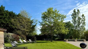 Eine Terrasse mit Sitzgelegenheiten im Freien, einem Rasen und einem Grill.
