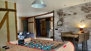 Ein Zimmer mit einer Kickeranlage, einem Essbereich mit Stühlen und einem Tisch sowie einem Wohnbereich mit einer Couch und einer Lampe.