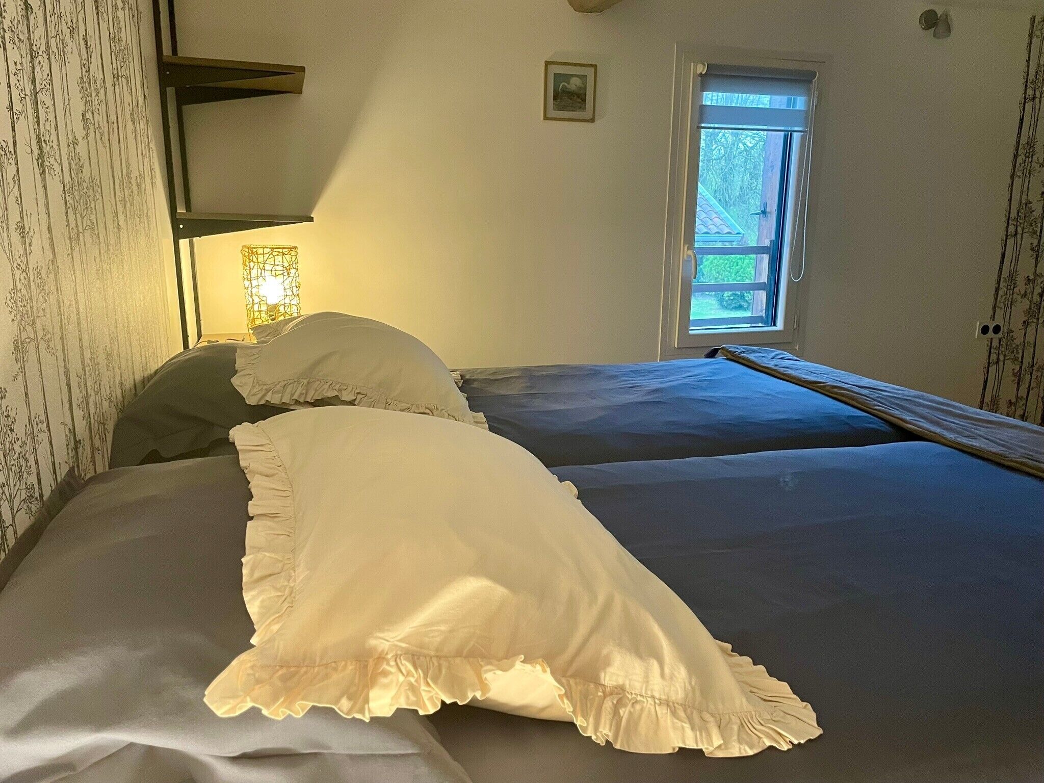Une chambre avec deux lits, une fenêtre donnant sur un beau paysage et une étagère fixée au mur.