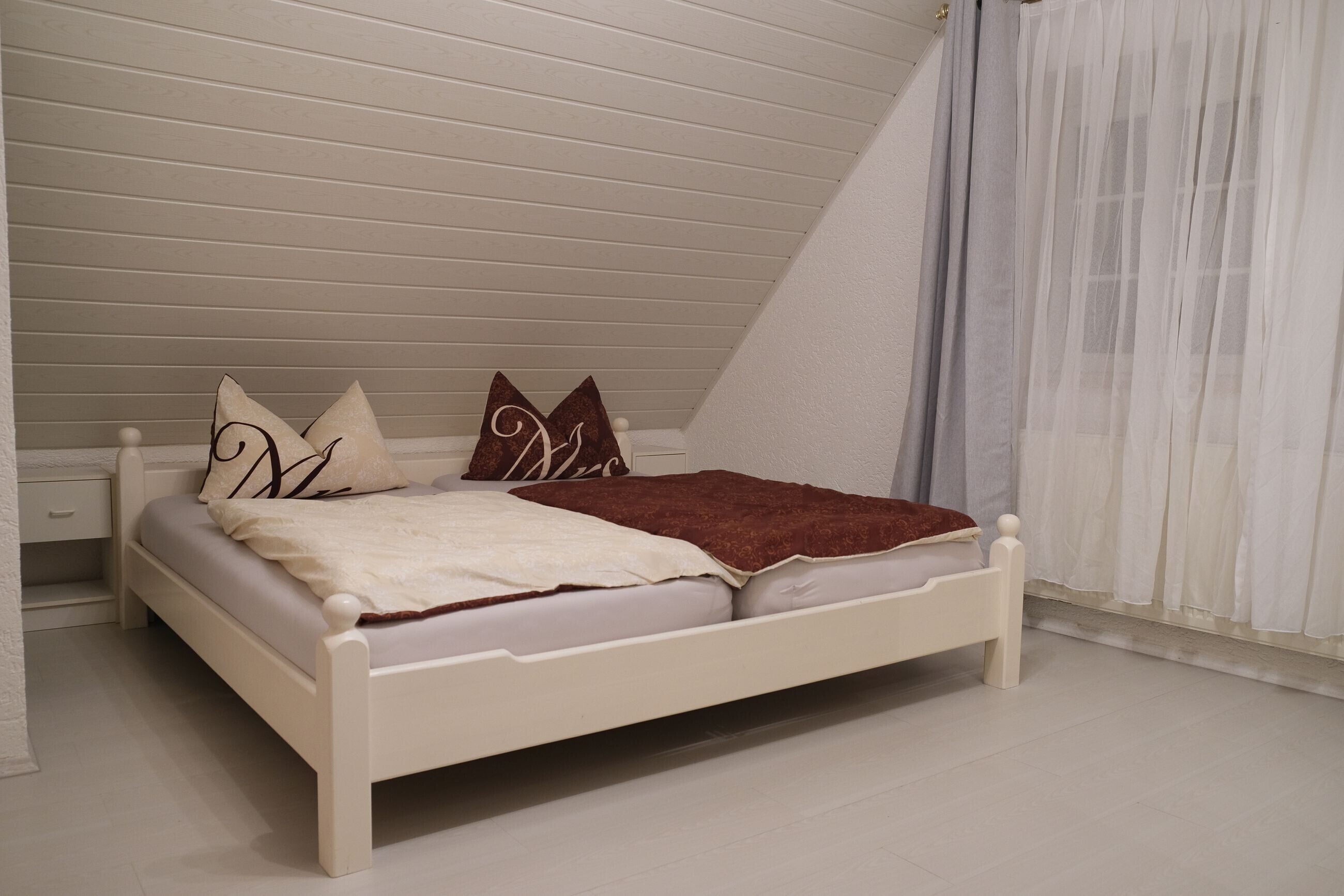 A white bed in a room with sloped ceilings and a white floor.