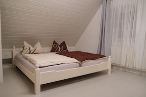 A white bed in a room with sloped ceilings and a white floor.