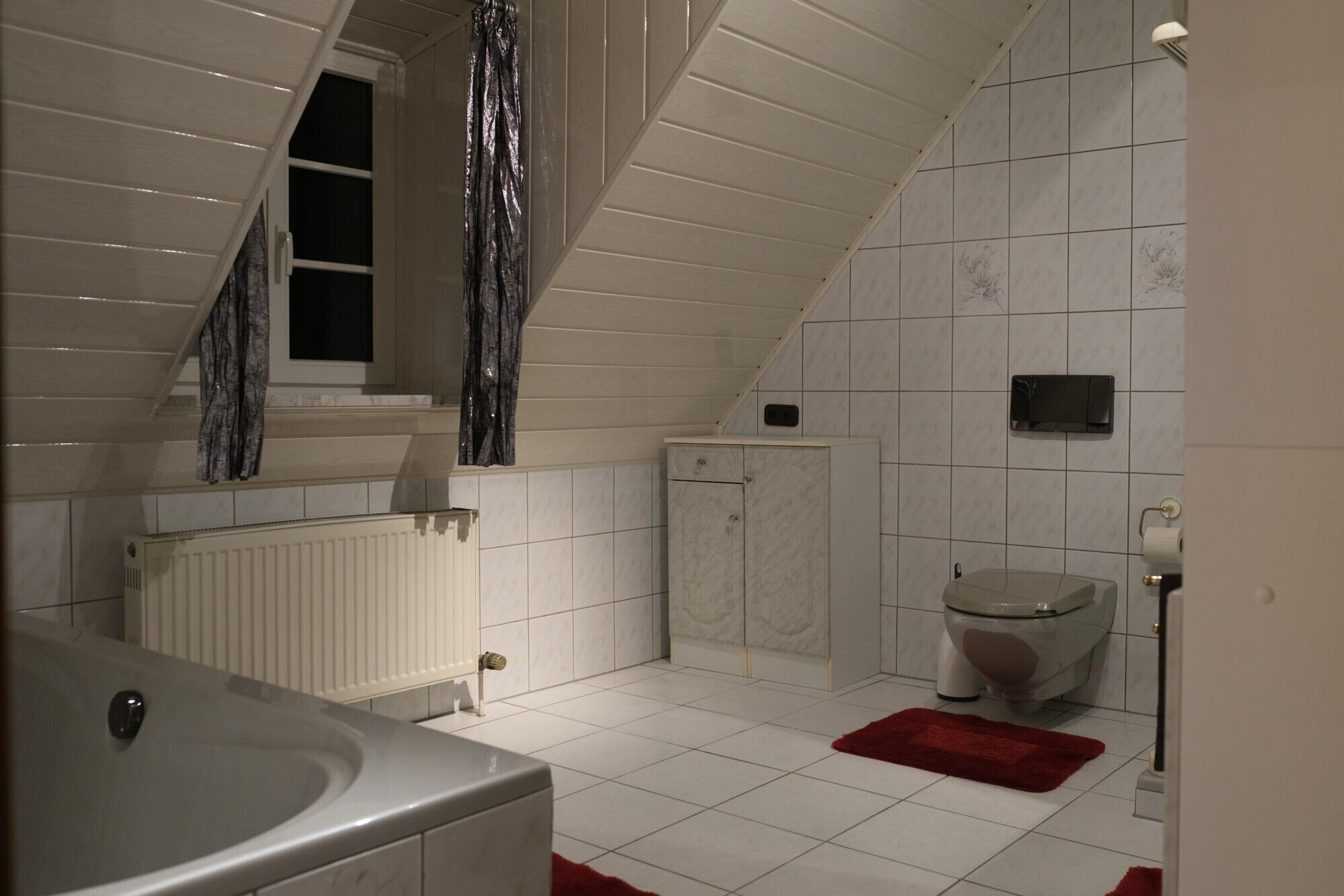 Un bagno con soffitto spiovente, un water, un termosifone e una tenda per la doccia.