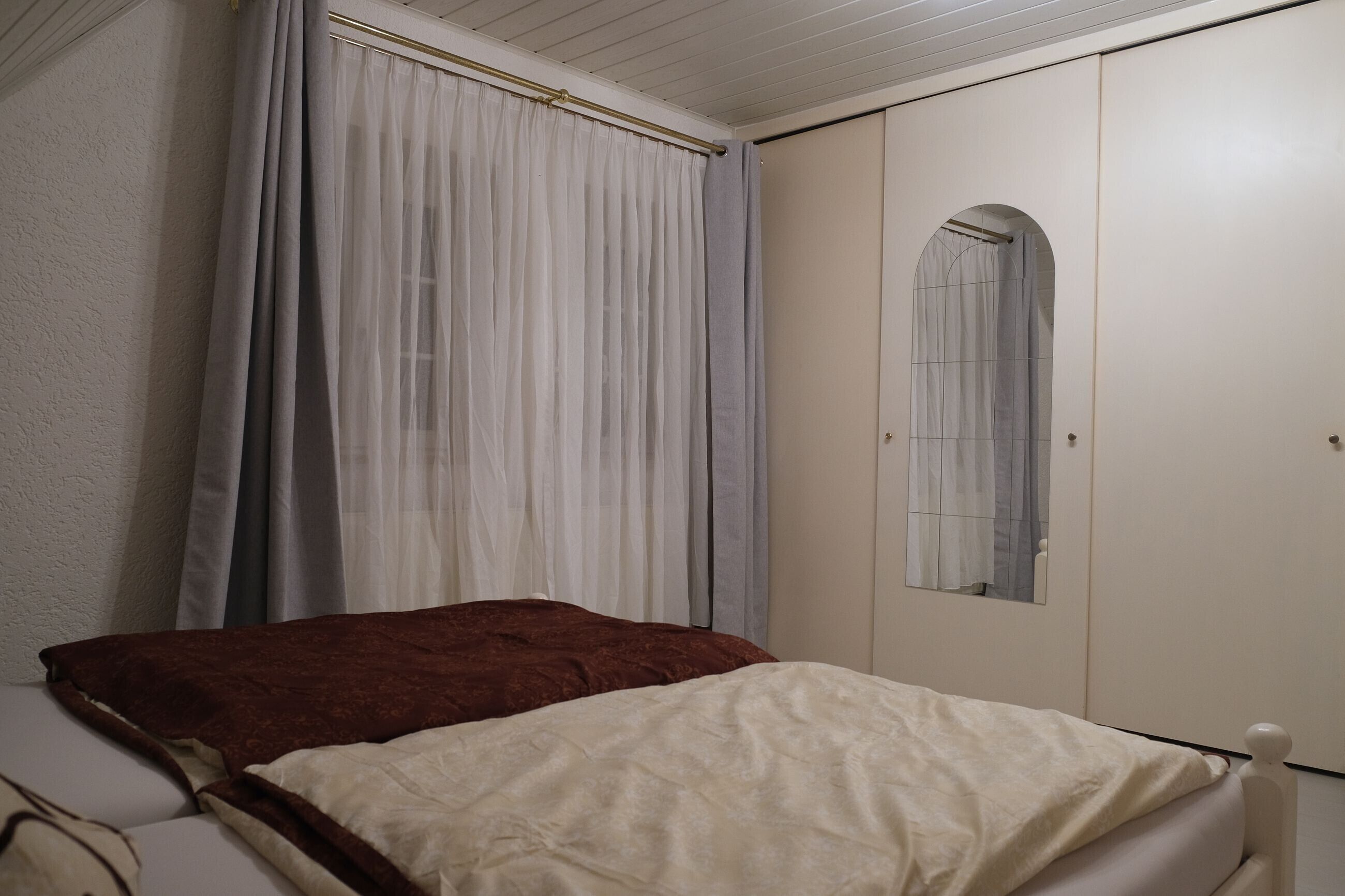 A bedroom with a bed, a wardrobe, and a mirror.