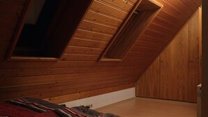 Een kamer met een schuine hemel, houten wanden, een bed met een gestreept dekbed en een deur.