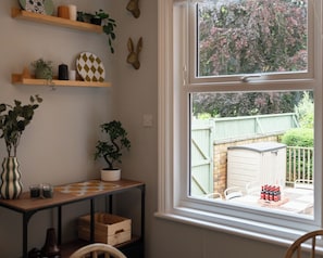 A room with a window, a wooden table with a vase and a potted plant, and a shelf with decorative items. - 59 Garfield Road (Scarborough)