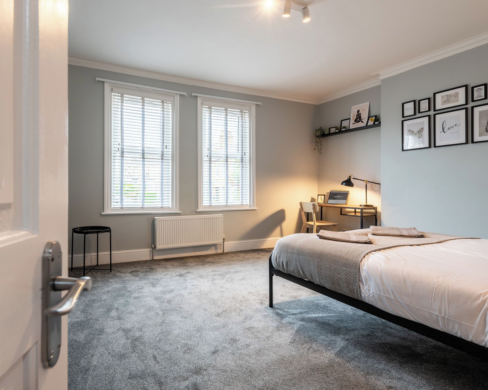 Ein Schlafzimmer mit einem Bett, einem Schreibtisch, einem Stuhl und zwei Fenstern mit Jalousien.