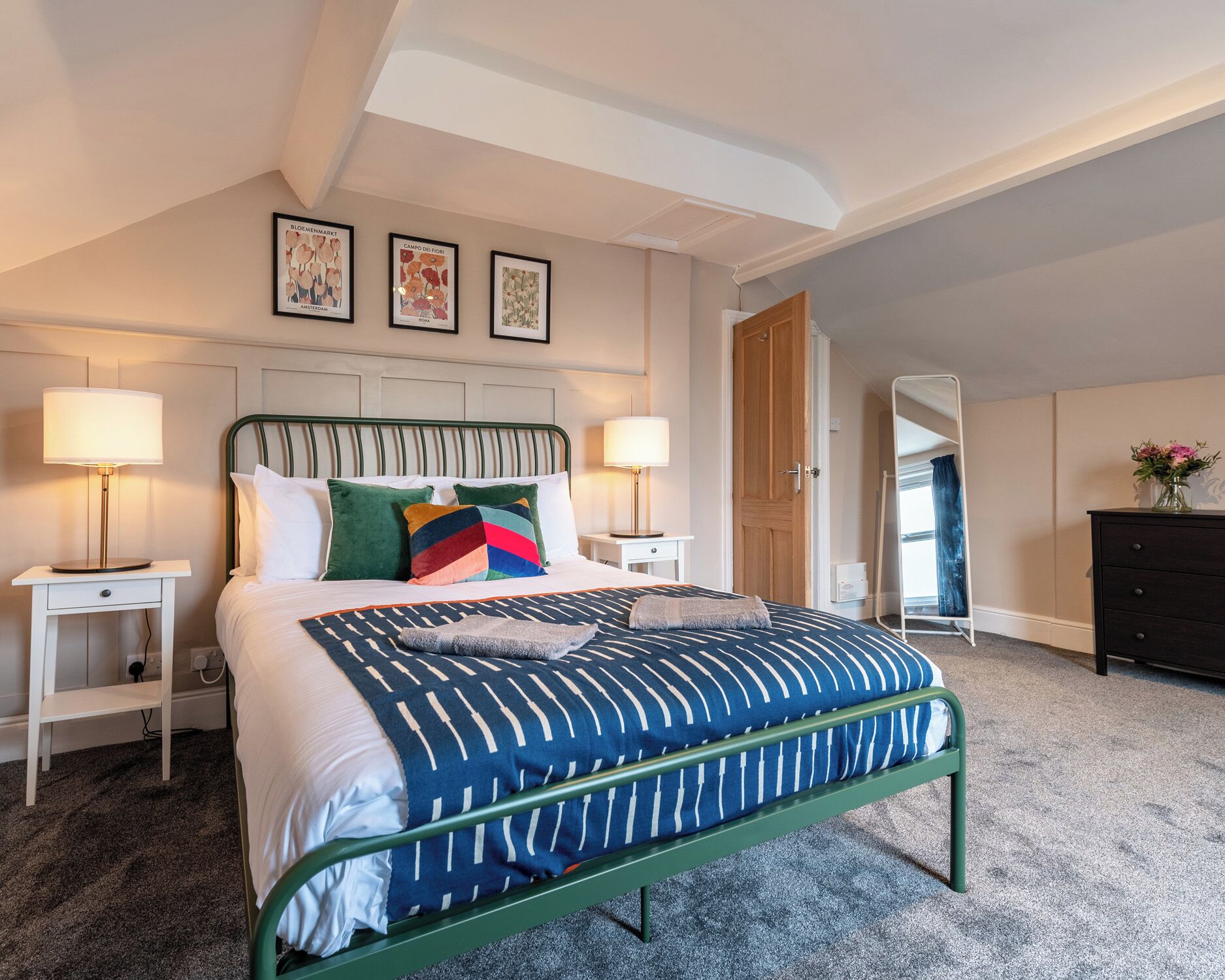 A hotel room with a bed, two bedside tables, a nightstand, a dresser, and a mirror.