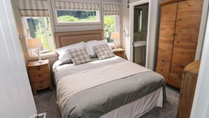 A bedroom with a bed, nightstands, a wooden wardrobe, and a window with curtains. - Dales Retreat (Skipton)
