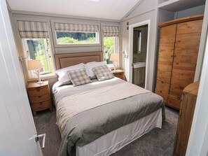 A bedroom with a bed, nightstands, a wooden wardrobe, and a window with curtains. - Dales Retreat (Skipton)