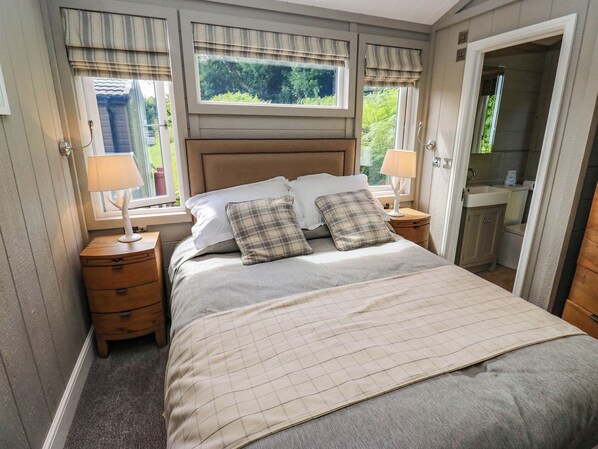 A bedroom with a bed, two bedside tables, a nightstand, a window with curtains, and a view of greenery outside. - Dales Retreat (Skipton)