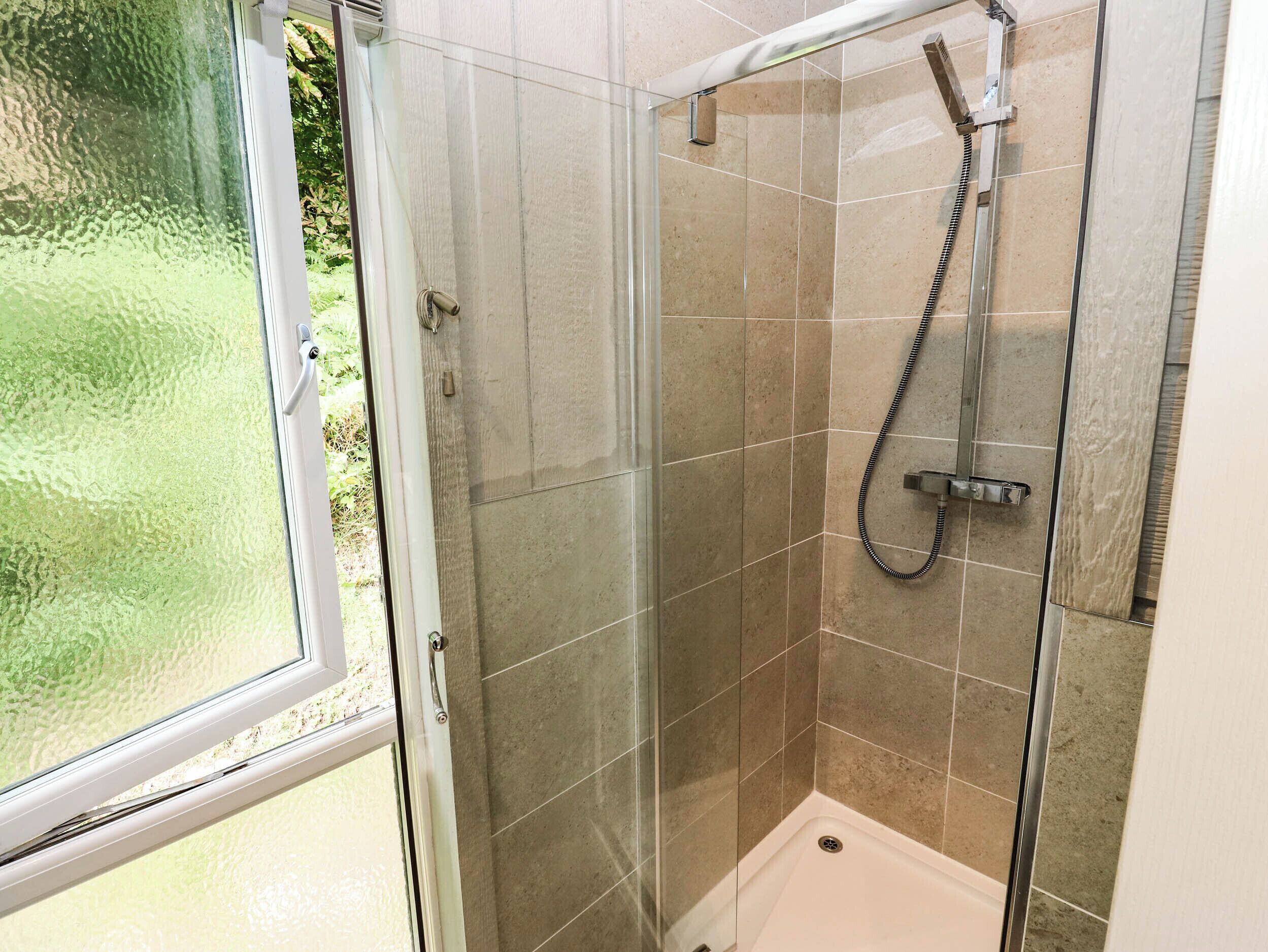 A shower with a handheld showerhead and a wall-mounted faucet, a glass door, and a tiled floor.