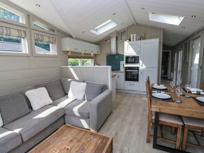 A modern kitchen with white cabinetry, a built-in oven, and a dining area with a wooden table set for four. - Dales Retreat (Skipton)