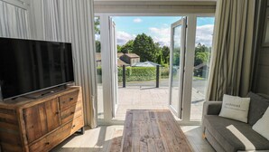 A living room with a television on a wooden cabinet, a sofa with a cushion, and a view through a glass door to the outside. - Dales Retreat (Skipton)