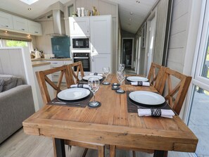 A dining table set for four with a view of the kitchen and a balcony. - Dales Retreat (Skipton)