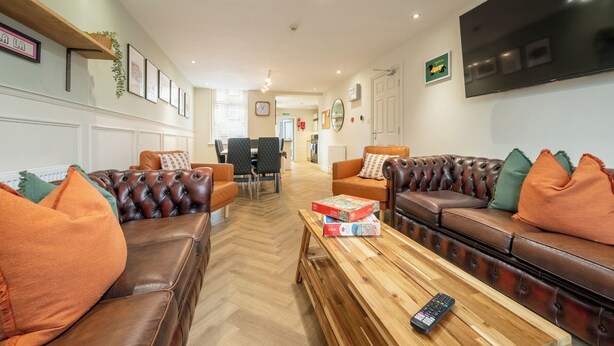 A spacious living area with leather sofas, a wooden coffee table, and a flat-screen TV mounted on the wall. - The Ravines (Scarborough)