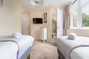 Quarto com duas camas, televisão, cômoda e banheiro visível por uma porta aberta.
