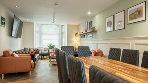 A dining area with a long wooden table and multiple chairs, a sofa, and a television mounted on the wall. - The Ravines (Scarborough)