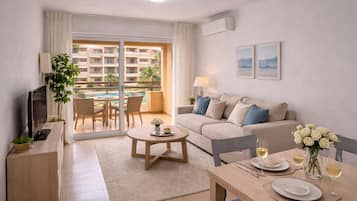 Una sala de estar moderna con un sofá, una mesa de centro, un televisor y un área de comedor con una mesa dispuesta para dos.