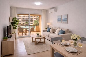 A modern living room with a sofa, a coffee table, a TV, and a dining area with a table set for two. - Deluxe 2-Bedroom Apartment (El Ejido)
