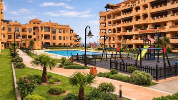 Un edificio residencial con piscina, parque infantil y un jardín bien cuidado.