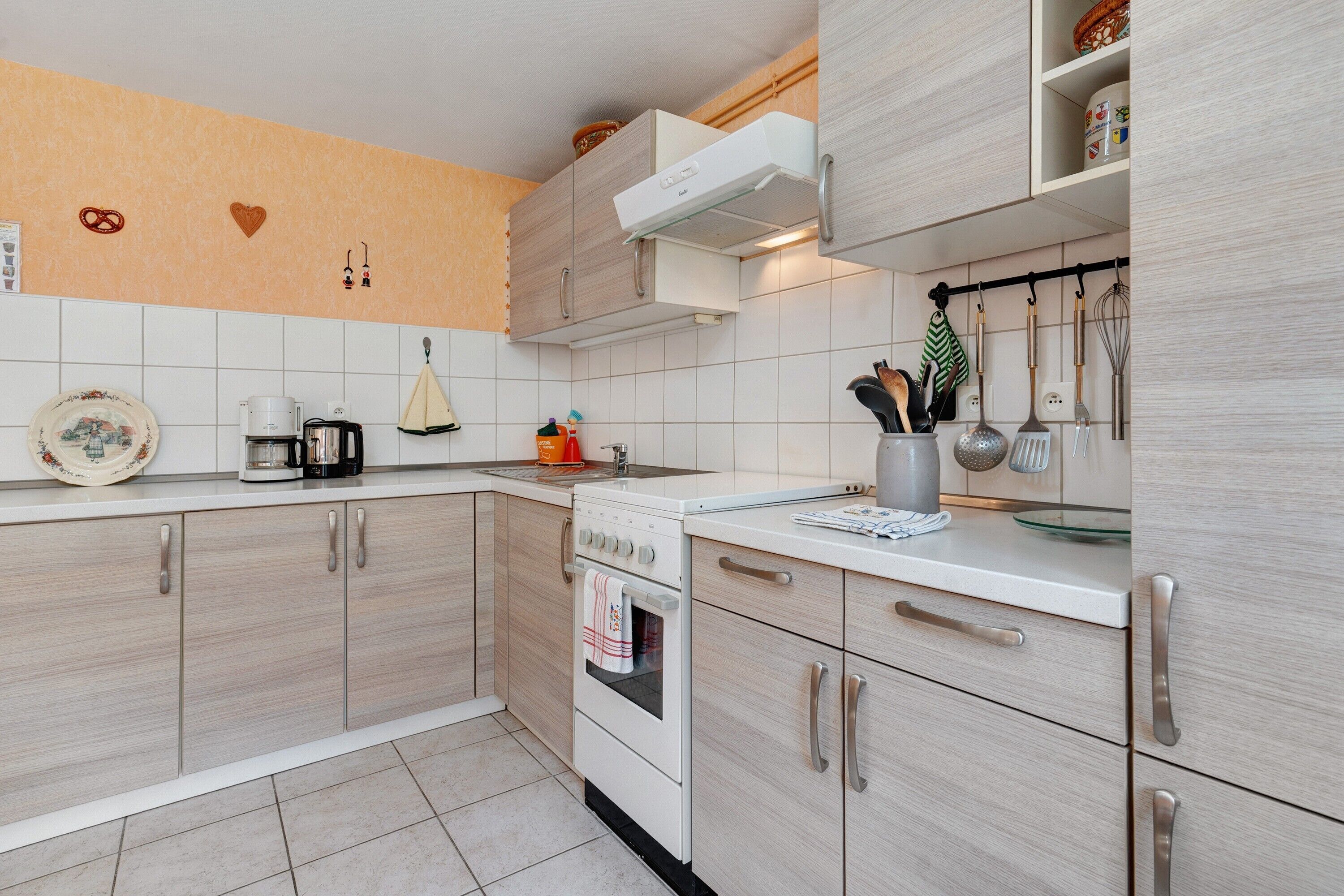 A modern kitchen with light wood cabinets, a white countertop, and a stainless steel range hood.
